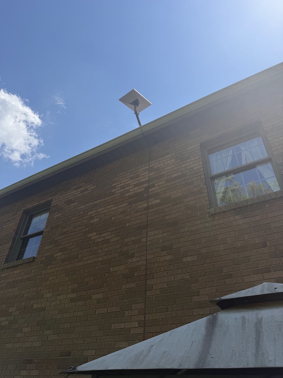 Starlink dish mounted above a brick home's roofline with exterior cable routing