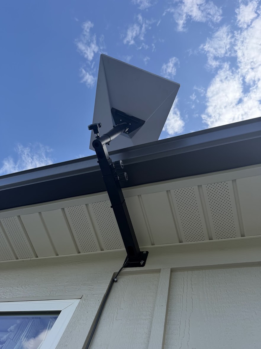 Starlink dish on an extended wall mount beneath a residential roofline