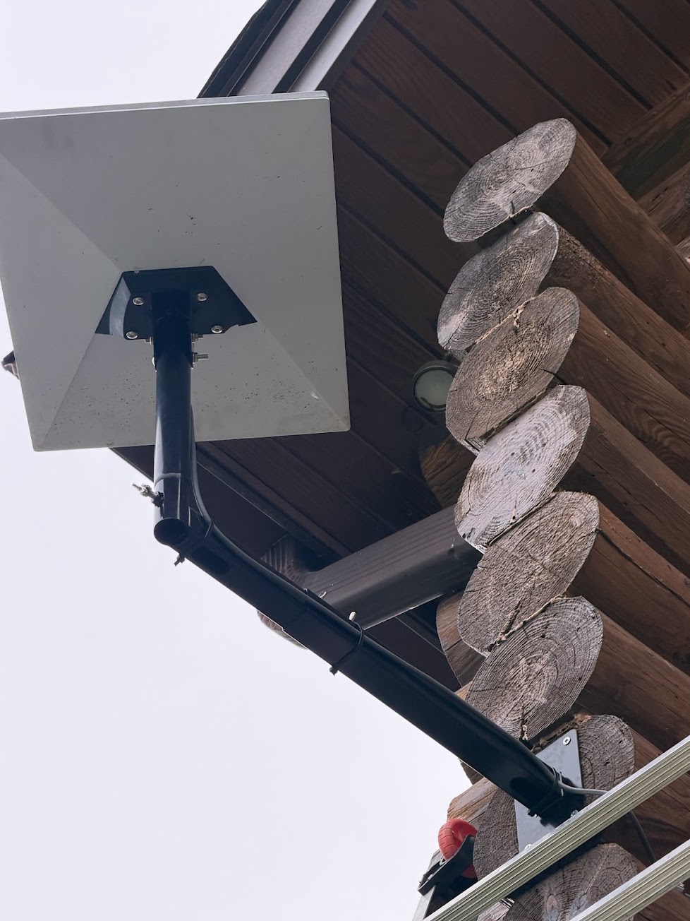 Starlink dish installed on an extended wall mount with clean cable routing along a log home